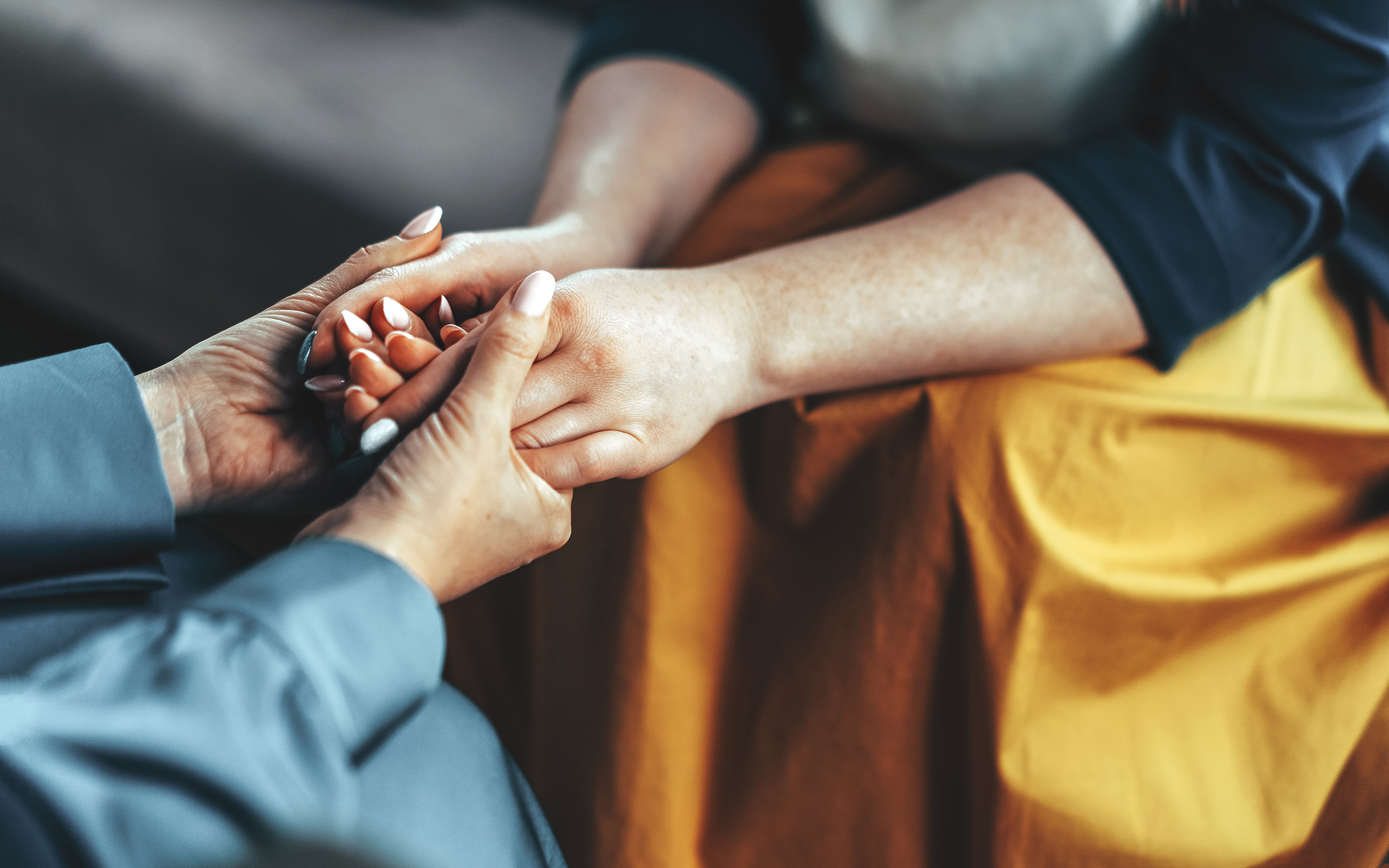 Close-up of two people's hands clasped together as they sit facing one another.