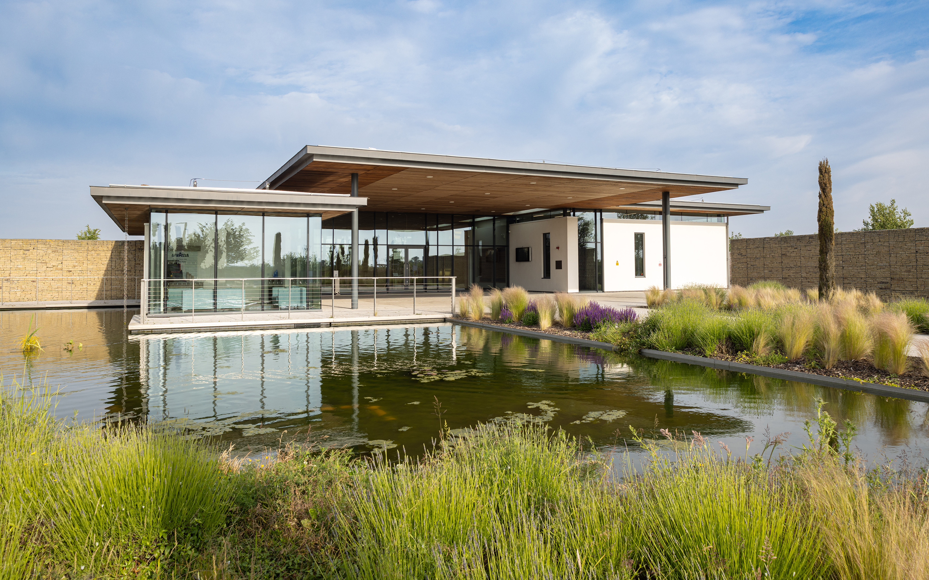 A modern glass-fronted building with a curved roof, reflected in an ornamental pond.